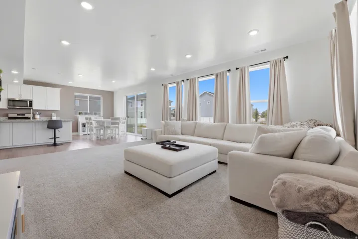 Open-concept living area with recessed lighting, large windows, light-toned carpet, a kitchen island with stone countertops, and wood-finish flooring