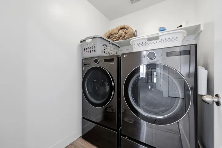 Dedicated laundry area featuring modern front-loading appliances, a built-in overhead shelf, and light wood-finish flooring