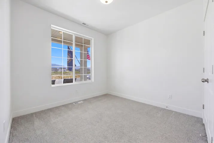 Room featuring light gray carpeting, crisp white walls, a multi-pane window, and a flush-mount ceiling light