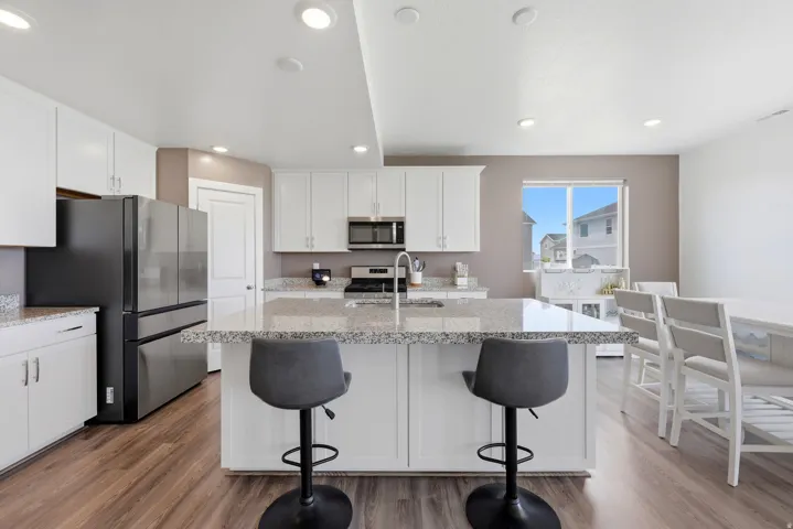 Kitchen featuring white shaker cabinetry, stainless steel appliances, speckled stone countertops, a central island with bar seating, and wood-finish flooring