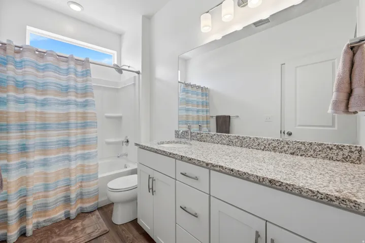 Bathroom featuring a white vanity with granite-style countertop, dual sinks, and white cabinetry with brushed nickel hardware