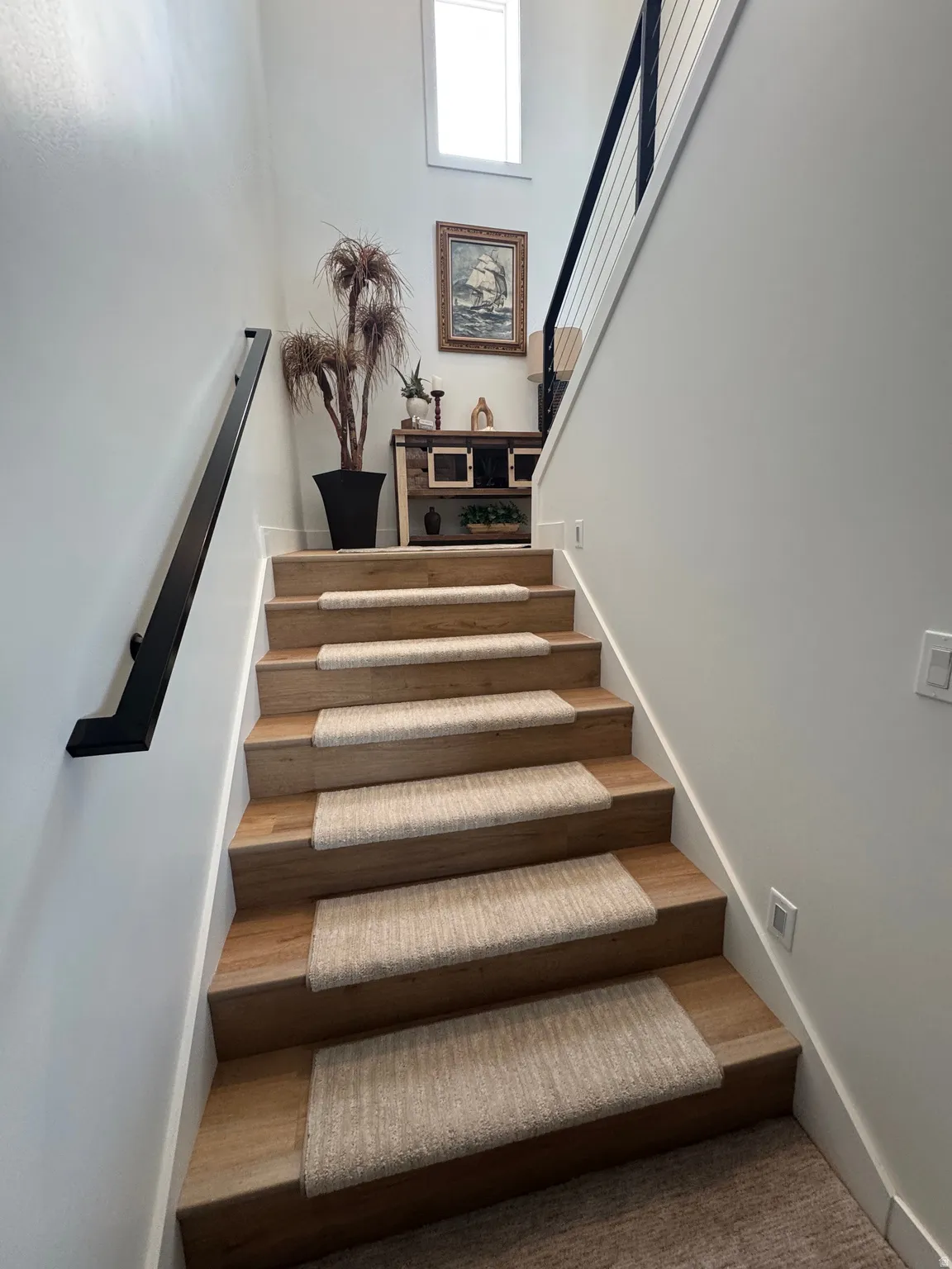 Staircase featuring wood-finish treads with carpet runners, a contemporary black metal handrail, and a black cable railing system