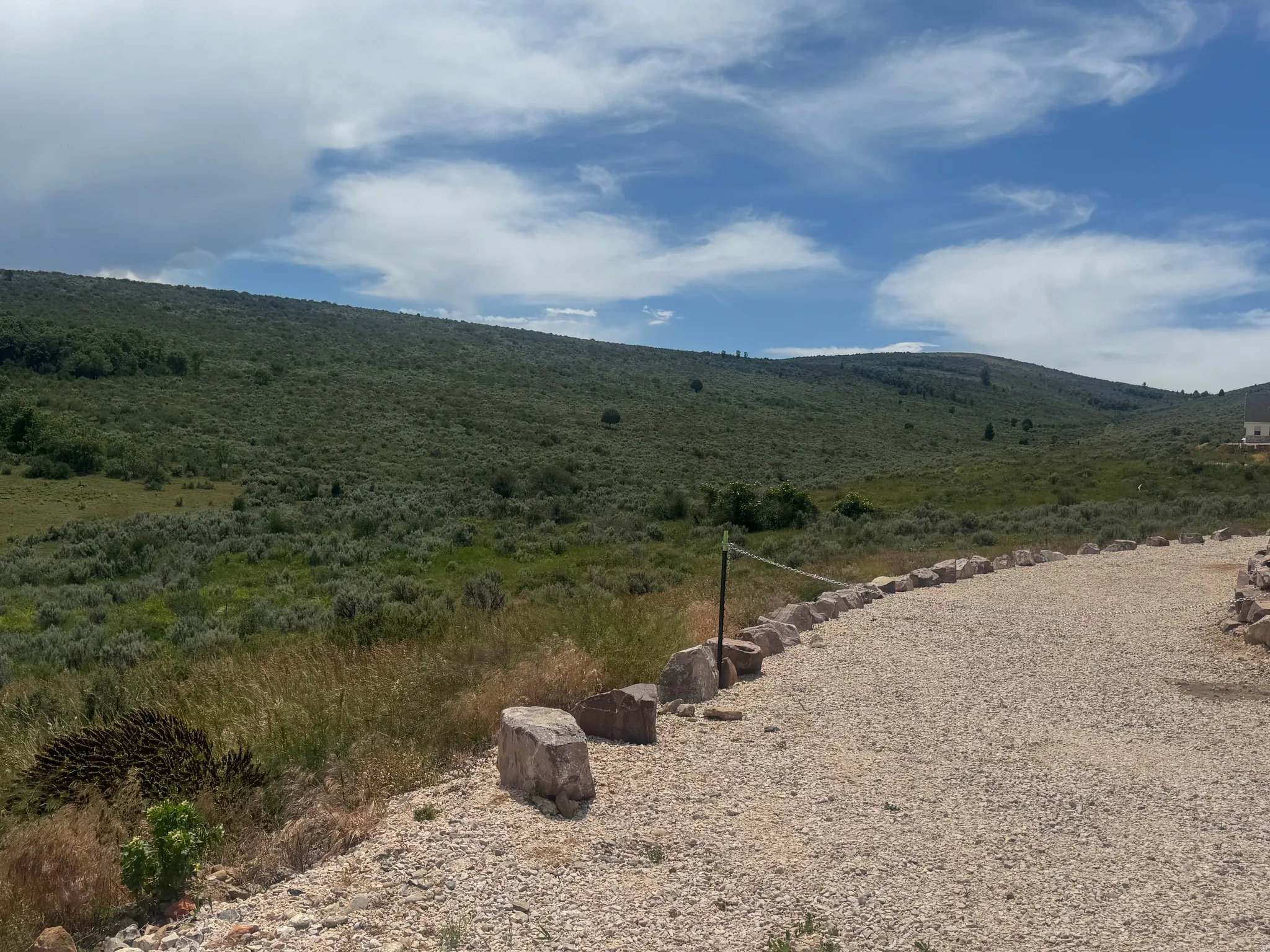 Gravel driveway bordered by natural stone, leading to expansive hillside terrain
