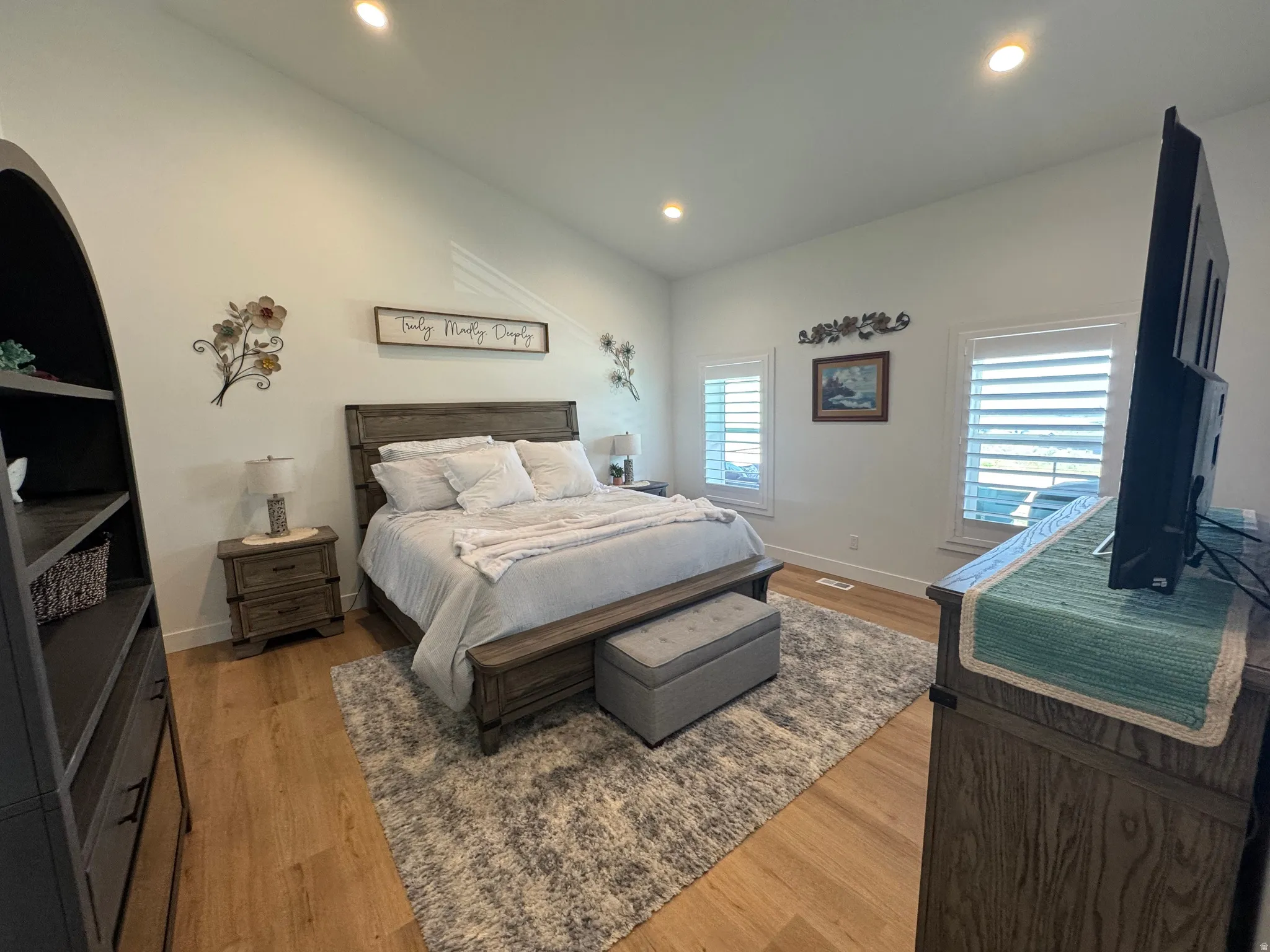 Vaulted ceilings enhance this room, featuring recessed lighting, wood-finish flooring, two windows with plantation shutters, and a built-in shelving unit