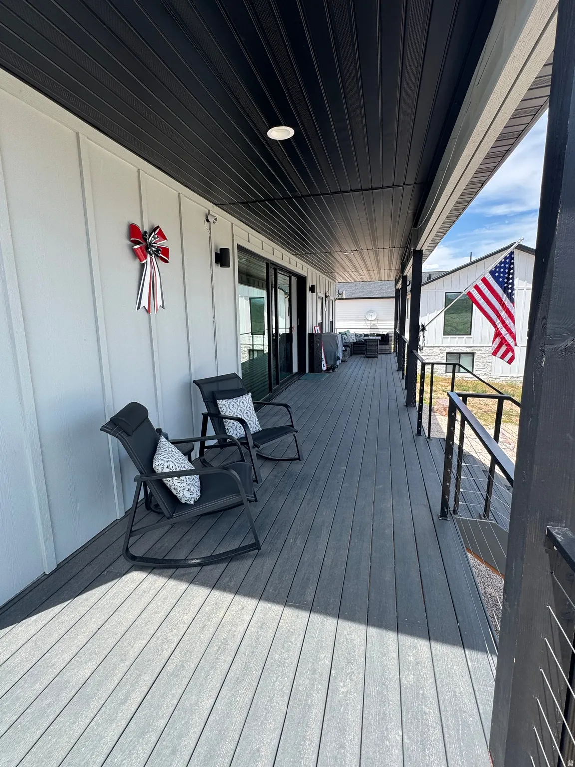 Covered outdoor patio featuring composite decking, recessed lighting, white vertical siding, and a black paneled ceiling