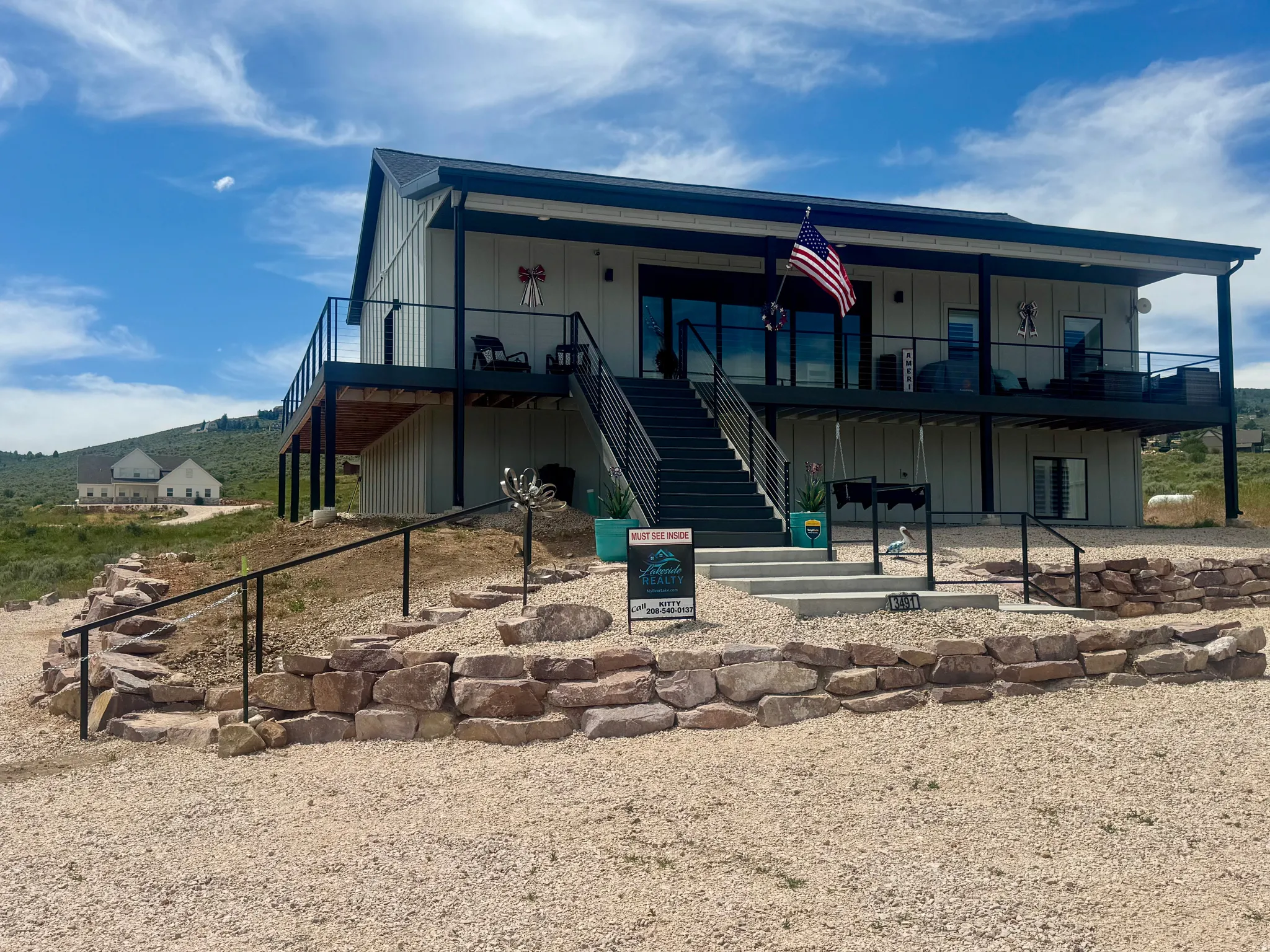 Modern farmhouse exterior with a covered upper-level deck, a covered ground-level patio, and a metal railing system