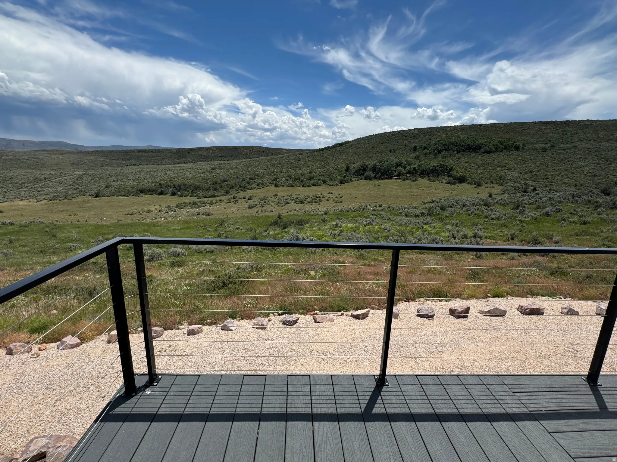 Outdoor deck with dark composite decking and a black metal cable railing system, overlooking a landscape of rolling hills and natural vegetation