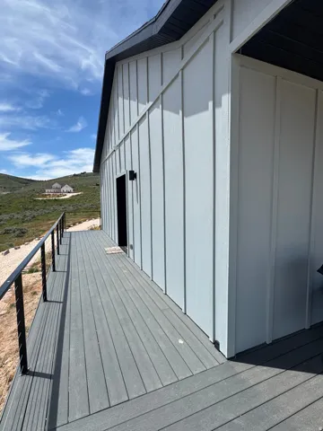 Board and batten siding, dark trim, and a dark composite deck with cable railing