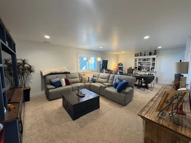 Expansive carpeted living area featuring recessed lighting, a built-in shelving unit, and a window with plantation shutters