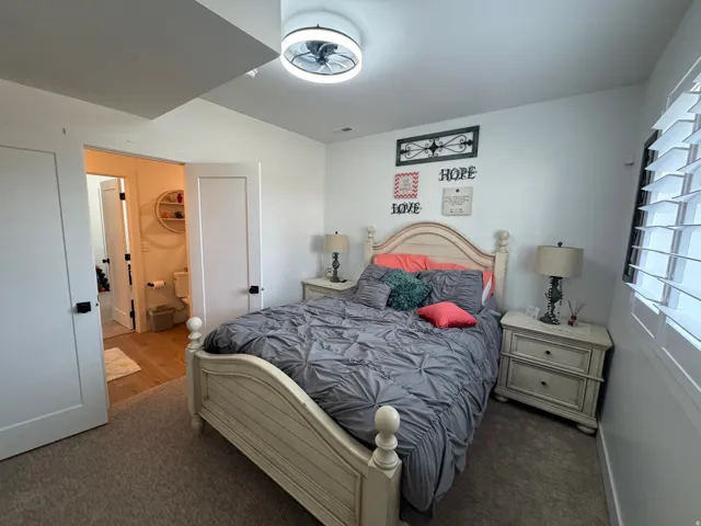 Bedroom featuring neutral carpeting, a ceiling fan with integrated lighting, and plantation shutters on the window