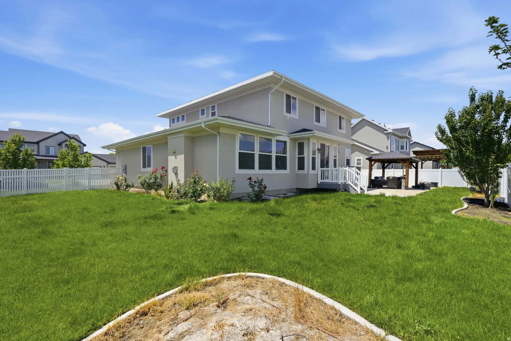 Spacious backyard featuring a large green lawn, a white picket fence, and a patio area with a pergola