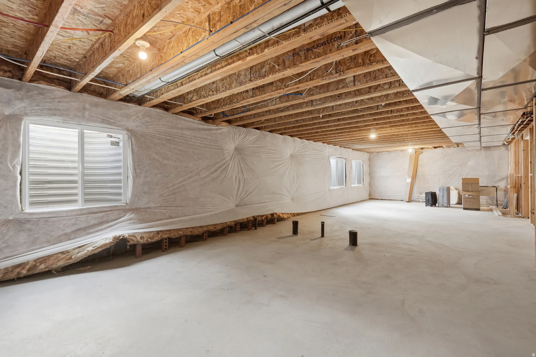 Unfinished basement featuring a concrete floor, exposed wood ceiling joists, and multiple egress windows