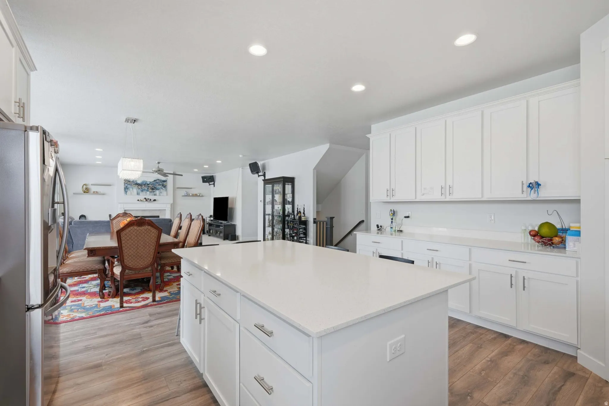 Expansive kitchen island with a light-colored countertop, white cabinetry, and wood-finish flooring