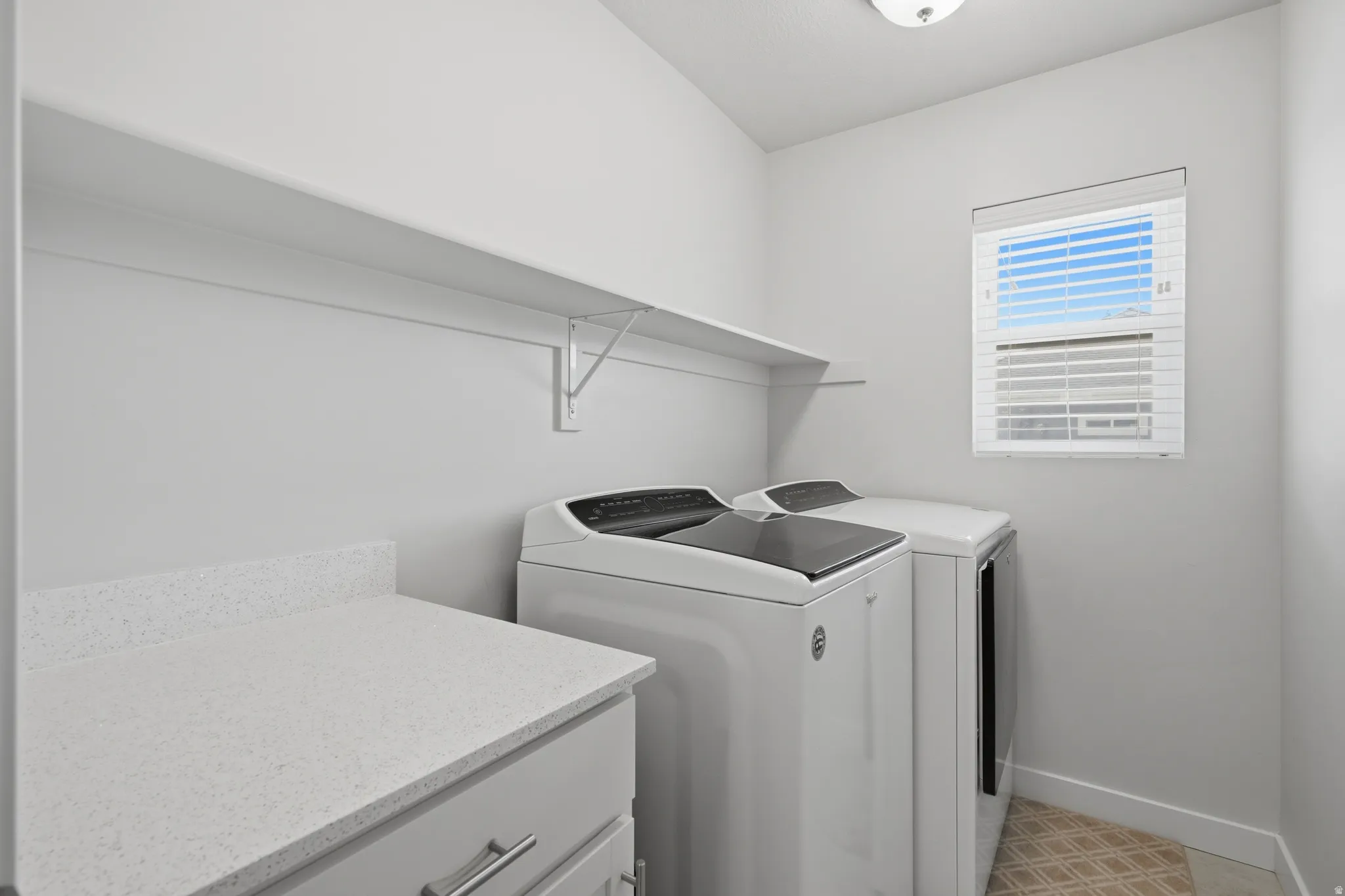 Utility room featuring upper shelving, a window with blinds, and light-toned flooring