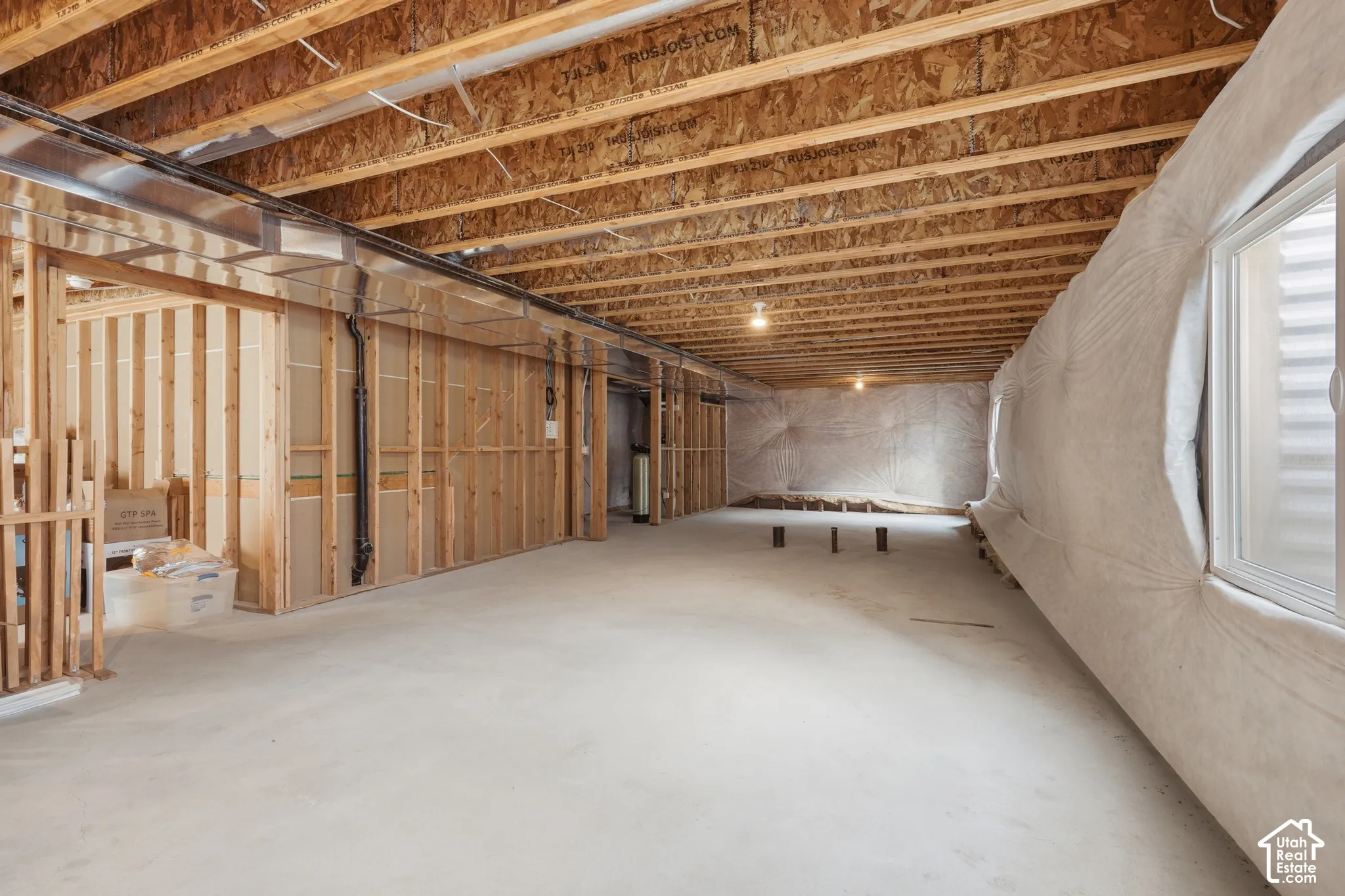 Spacious unfinished lower level featuring exposed wood joists, concrete flooring, framed wall sections, and an egress window