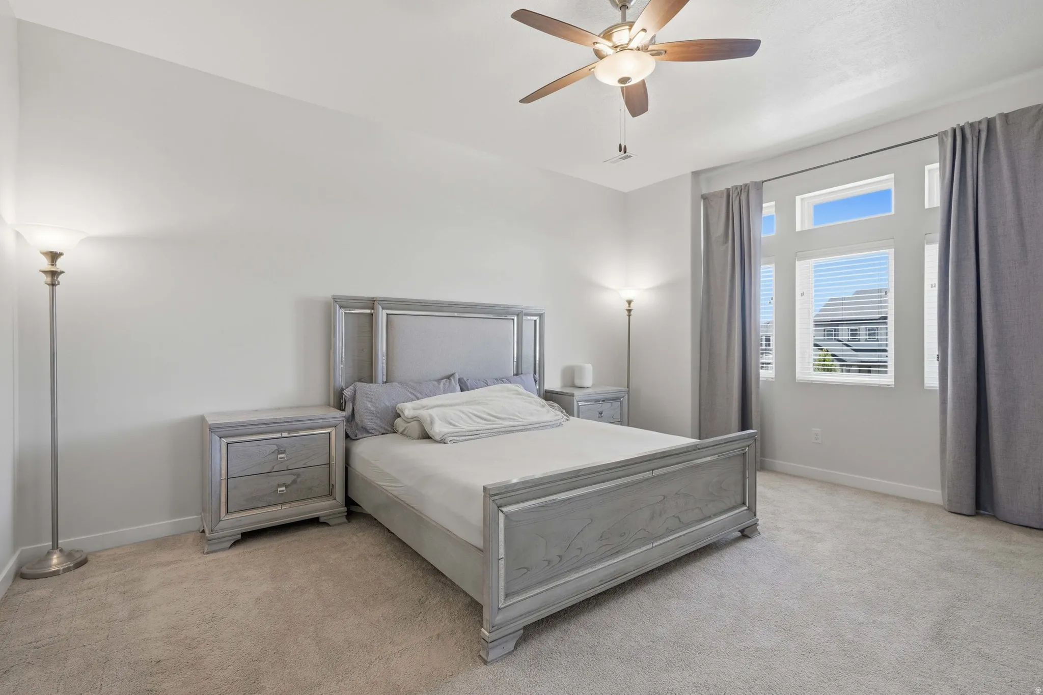 Spacious room featuring neutral carpeting, a ceiling fan with integrated lighting, and multiple windows with blinds and curtain rods