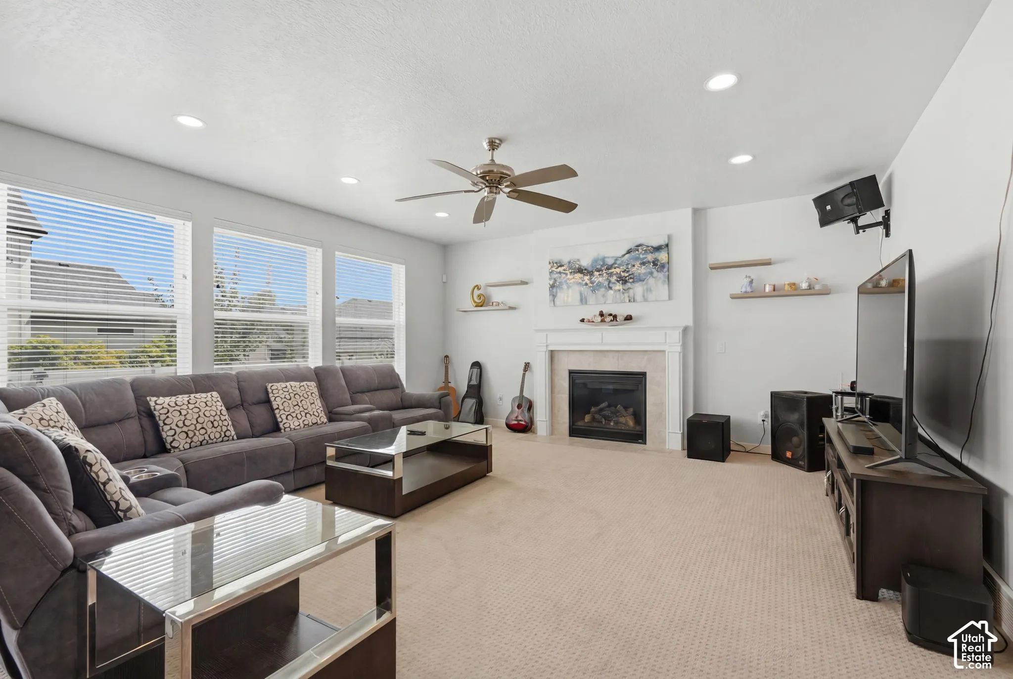 Spacious living area featuring a fireplace with a stone surround and a white mantel, complemented by recessed lighting and a ceiling fan