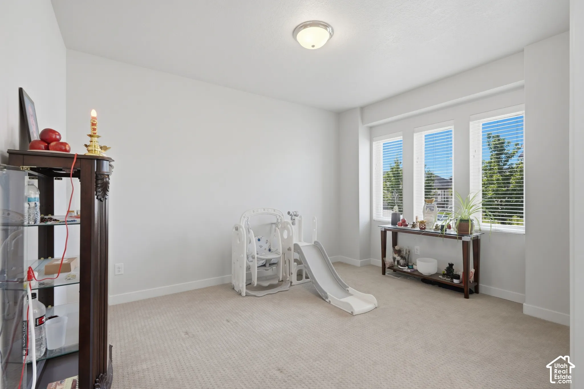 Bright room featuring three tall windows with horizontal blinds, neutral carpeting, and white walls