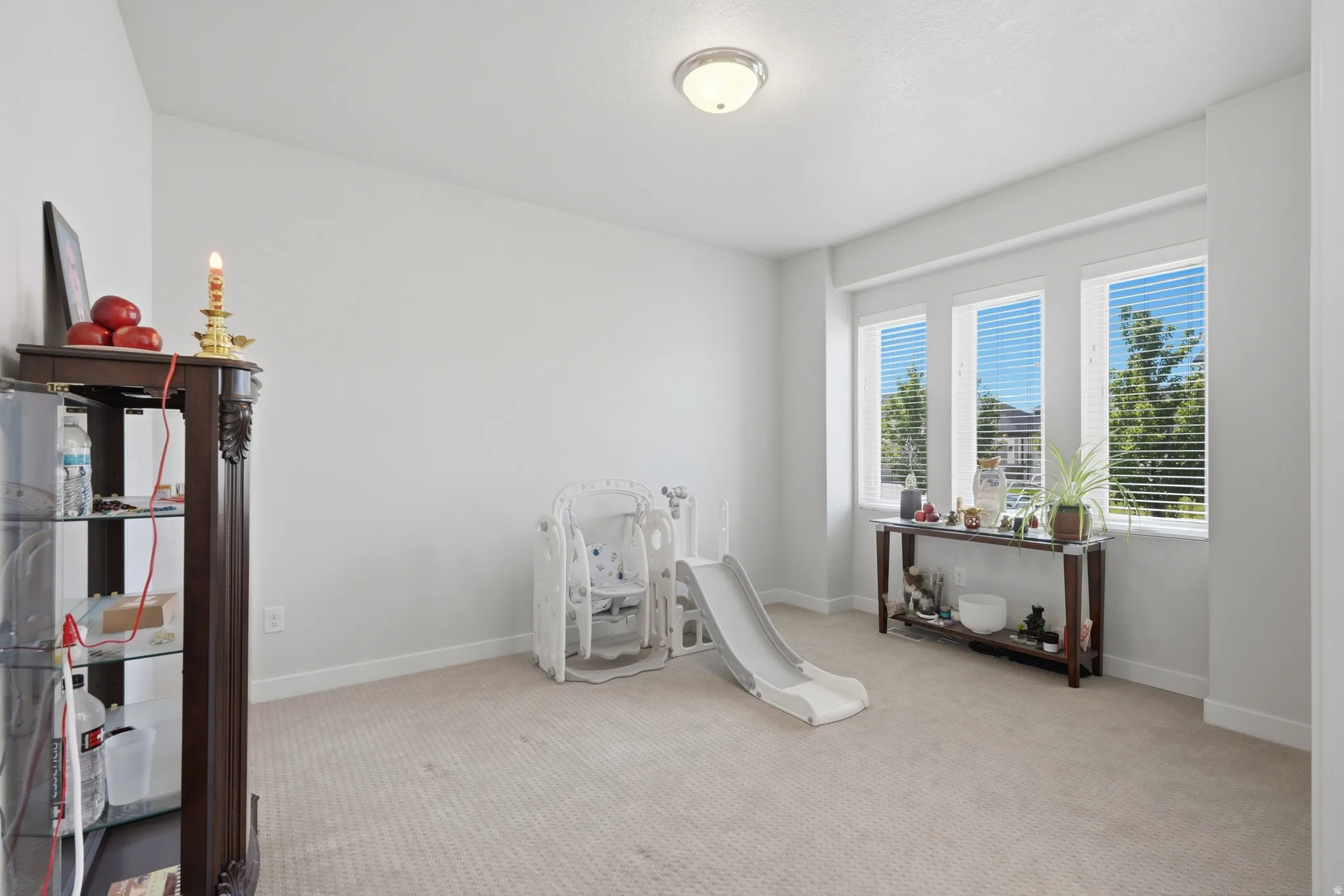 Bright room featuring three tall windows with horizontal blinds, neutral carpeting, and white walls
