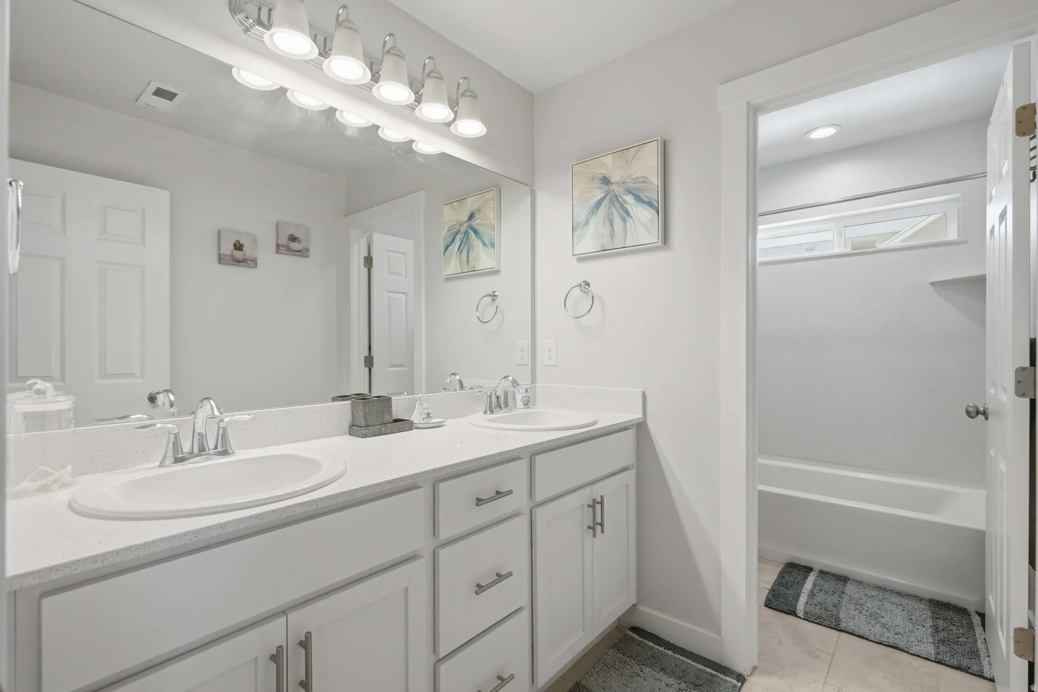 Double vanity with integrated sinks, white cabinetry, chrome hardware, and a large wall-mounted mirror