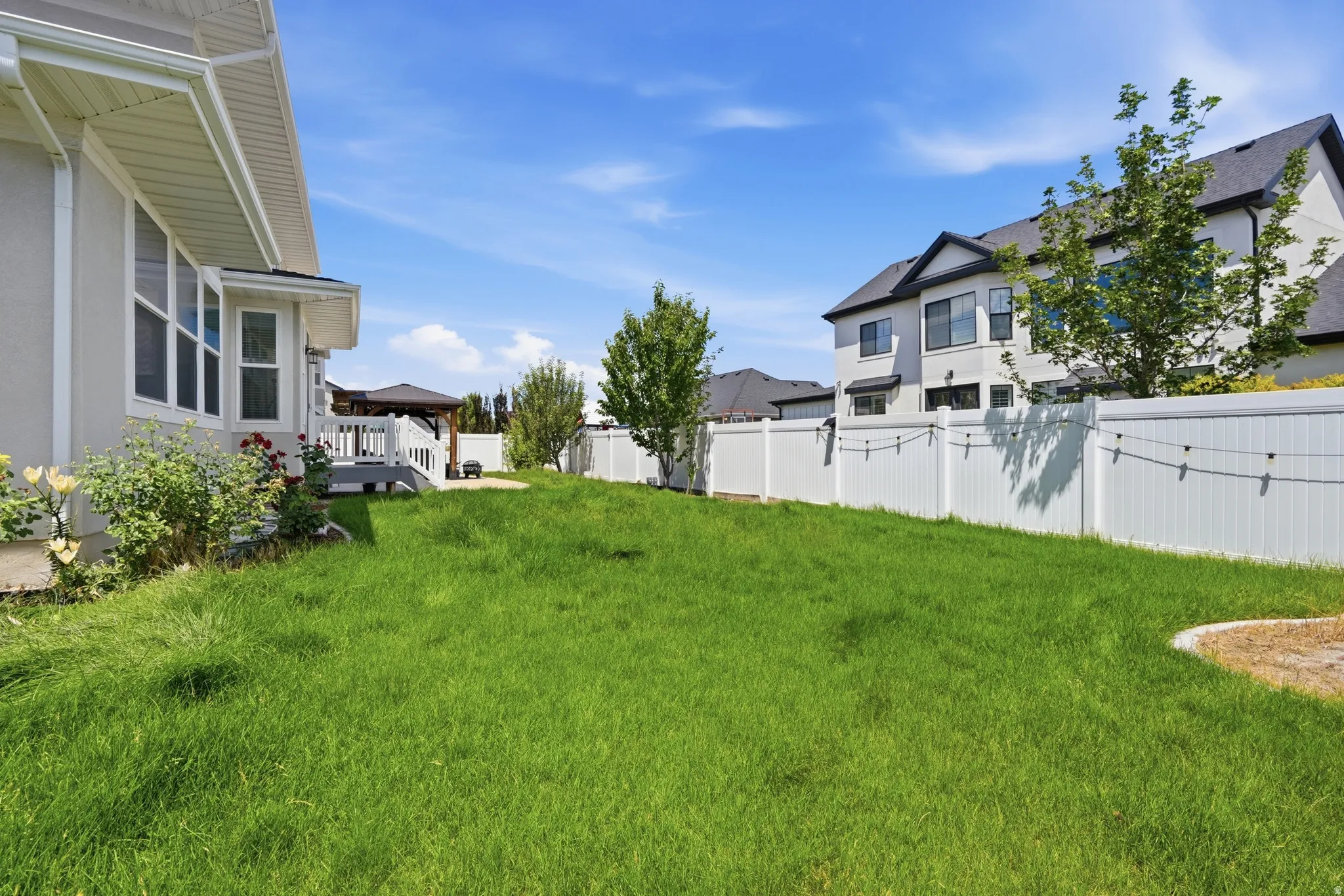 Expansive grassy yard with white vinyl fencing and string lighting