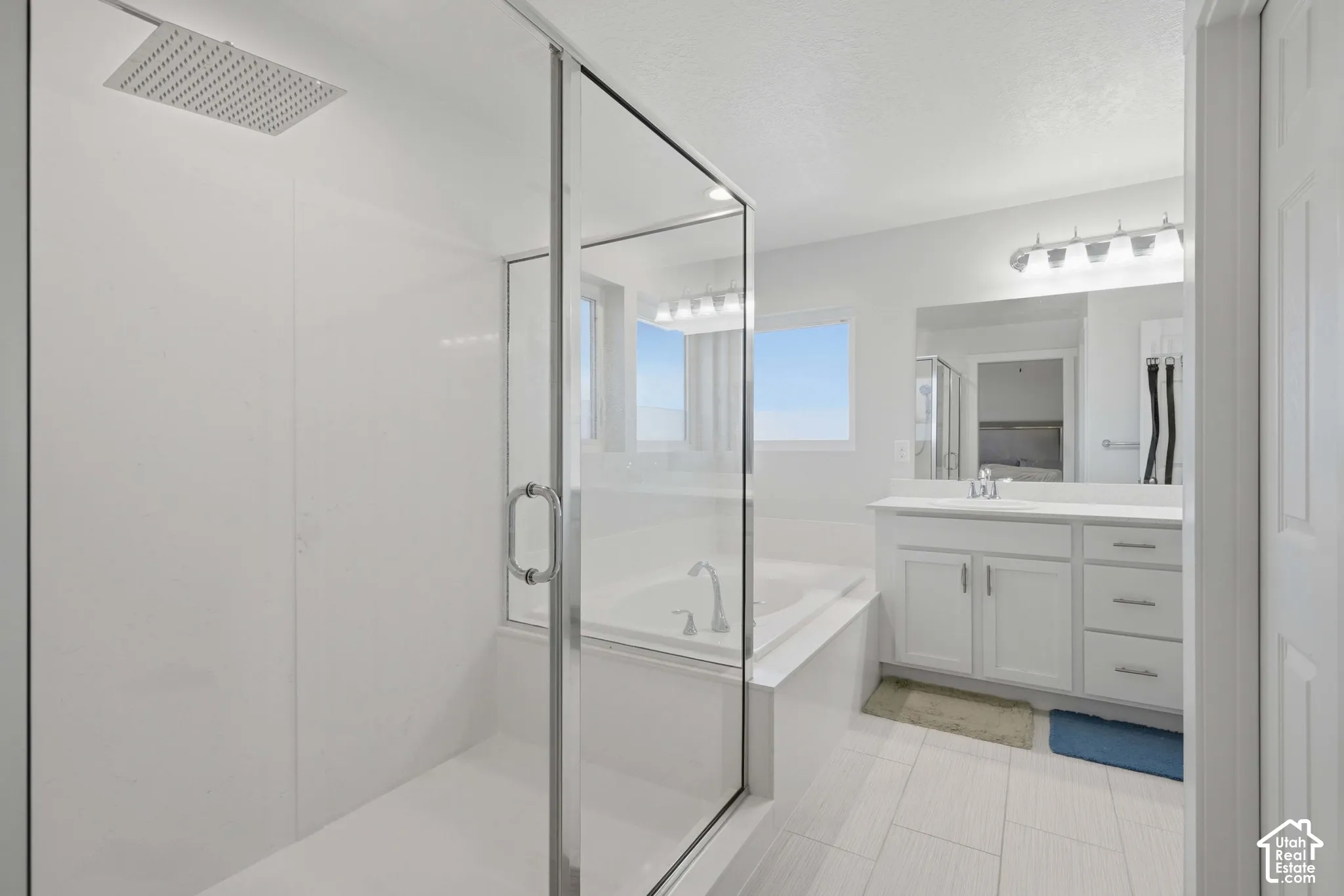 Spacious bathroom featuring a glass-enclosed shower with a rain shower head, a separate soaking tub, a single vanity with a white countertop and base cabinetry, and light-toned tile flooring