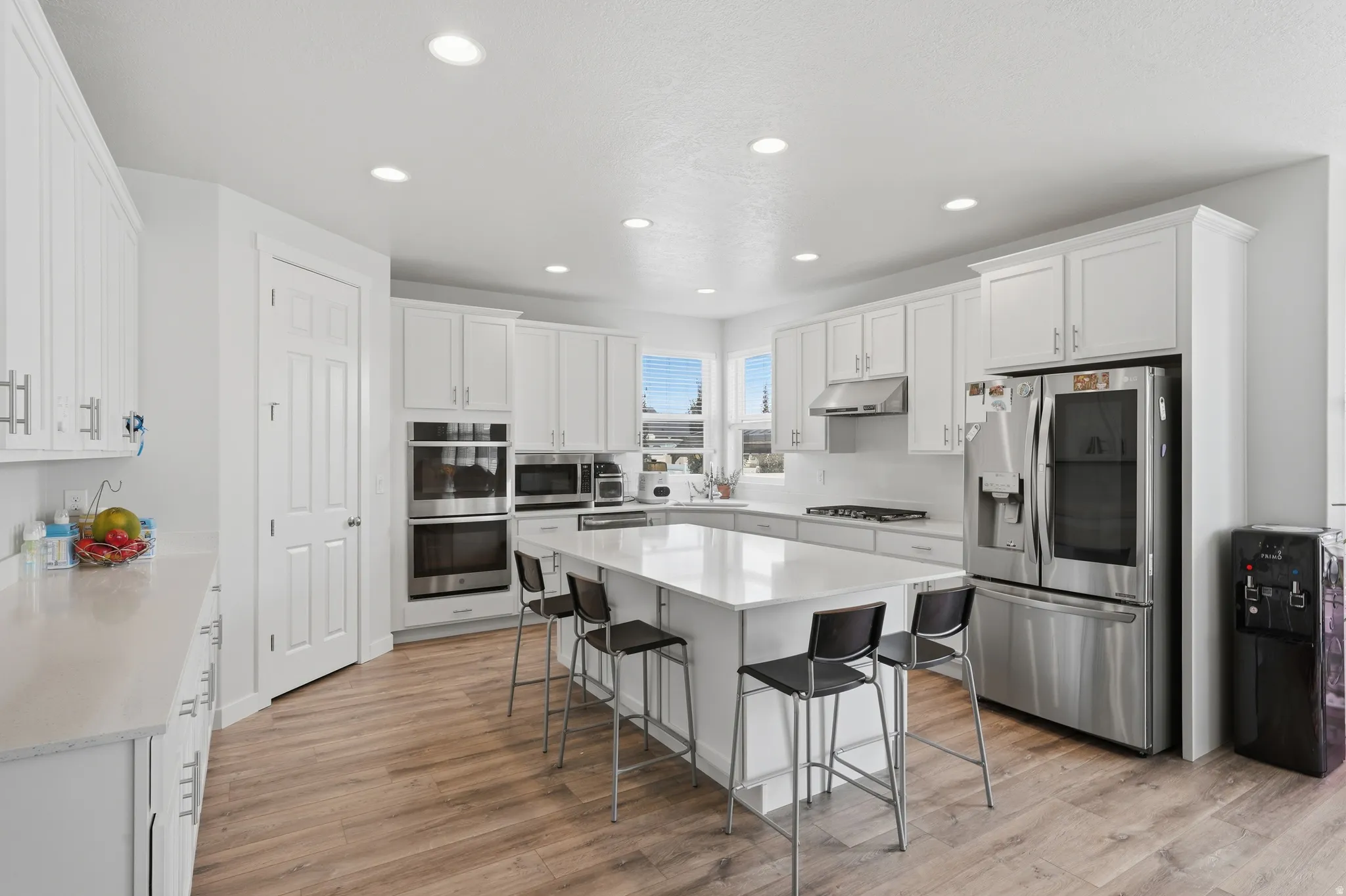 Modern kitchen featuring white cabinetry, light-toned countertops, wood-finish flooring, recessed lighting, and stainless steel appliances