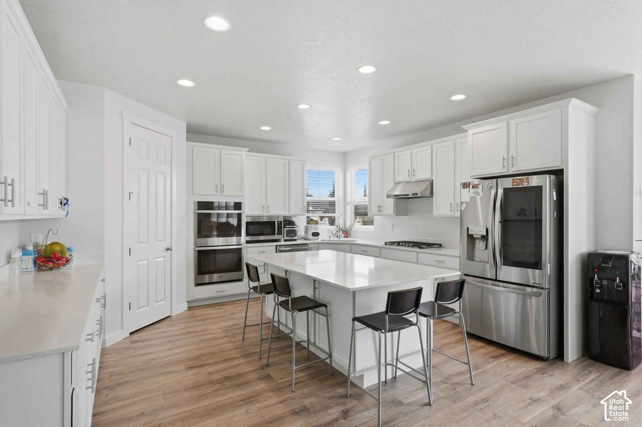 Modern kitchen featuring white cabinetry, light-toned countertops, wood-finish flooring, recessed lighting, and stainless steel appliances