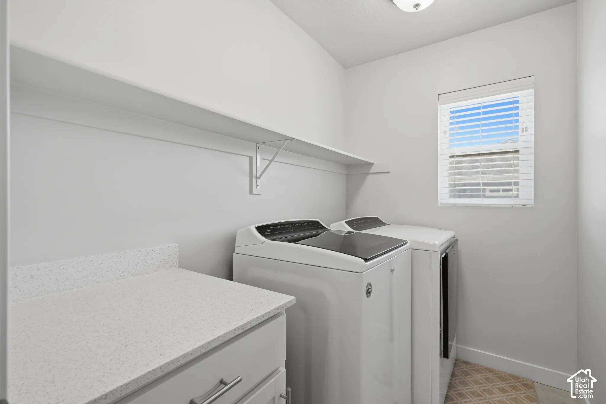 Utility room featuring upper shelving, a window with blinds, and light-toned flooring