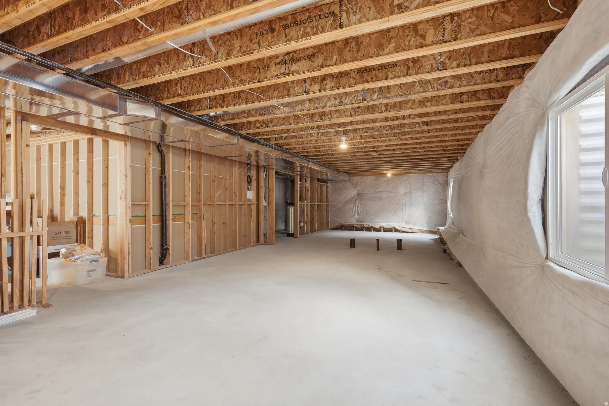 Spacious unfinished lower level featuring exposed wood joists, concrete flooring, framed wall sections, and an egress window