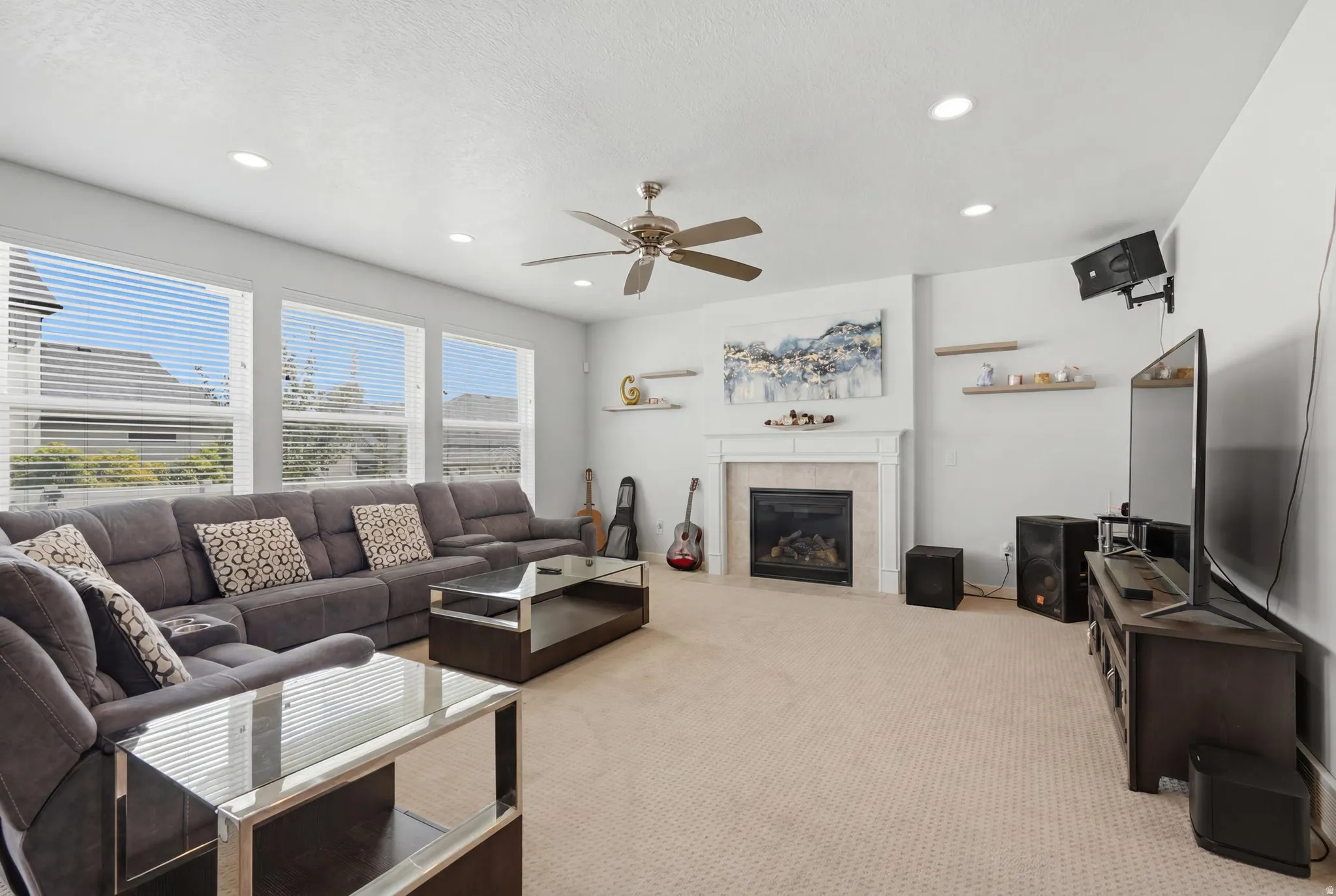Spacious living area featuring a fireplace with a stone surround and a white mantel, complemented by recessed lighting and a ceiling fan