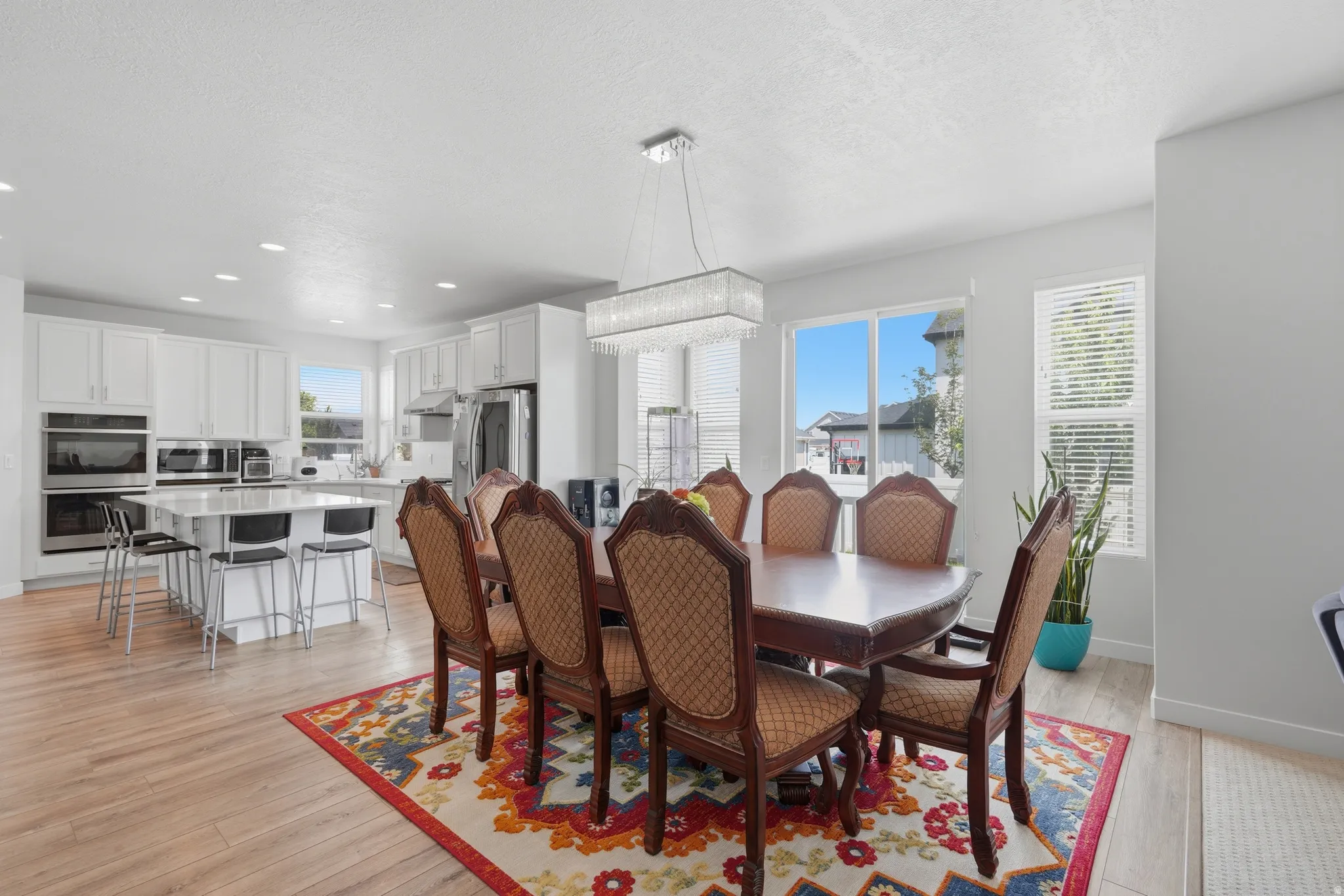 Open-concept dining area with wood-finish flooring, a contemporary chandelier, and large windows with blinds