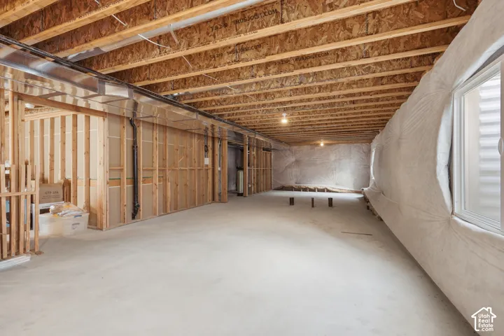 Spacious unfinished lower level featuring exposed wood joists, concrete flooring, framed wall sections, and an egress window