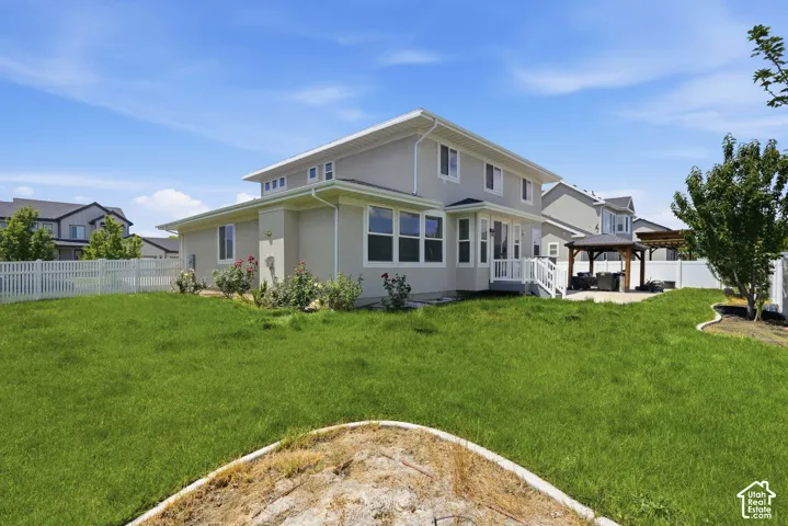 Spacious backyard featuring a large green lawn, a white picket fence, and a patio area with a pergola