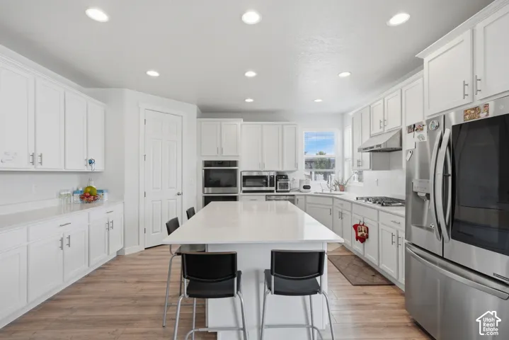 Bright kitchen featuring white shaker cabinetry, stainless steel appliances, a large center island with seating, recessed lighting, and wood-finish flooring
