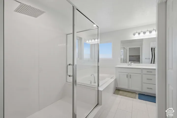 Spacious bathroom featuring a glass-enclosed shower with a rain shower head, a separate soaking tub, a single vanity with a white countertop and base cabinetry, and light-toned tile flooring