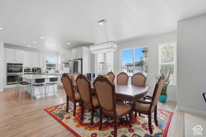 Open-concept dining area with wood-finish flooring, a contemporary chandelier, and large windows with blinds