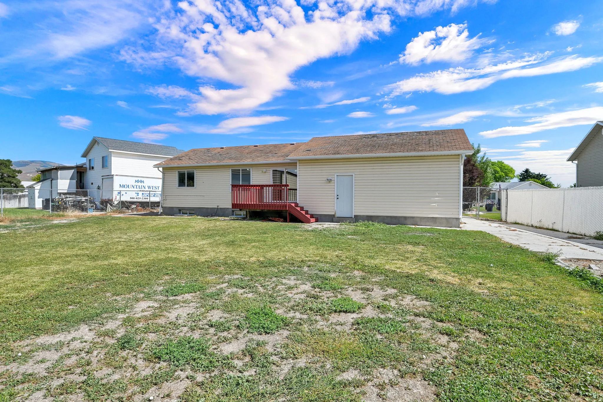 Expansive backyard featuring a deck with red-painted railings and stairs, a paved driveway, and a white privacy fence