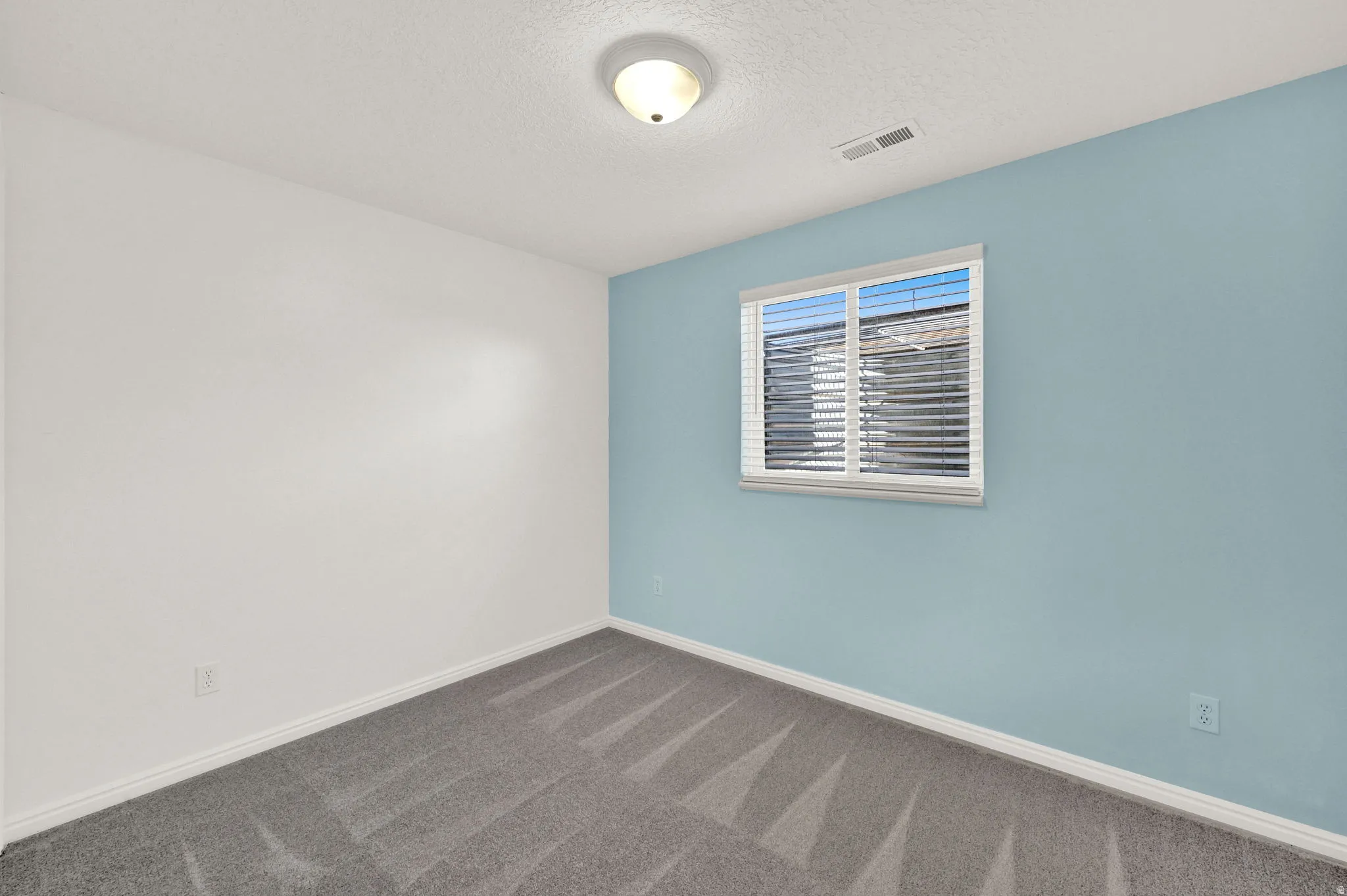 Room featuring two-tone wall paint, a single window with horizontal blinds, and a flush-mount ceiling light fixture