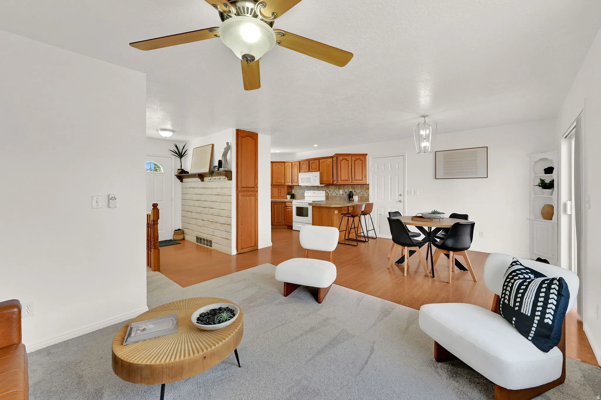 Open-concept living space featuring wood-finish flooring, a ceiling fan with integrated lighting, and a dining area illuminated by a decorative pendant light