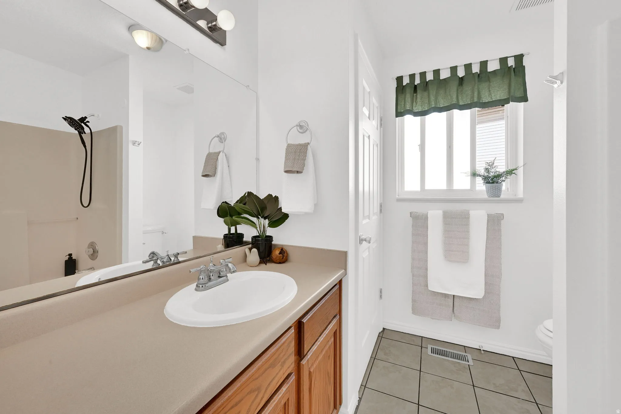 Bathroom vanity featuring an integrated sink, wood-finish cabinetry, and an expansive wall-mounted mirror