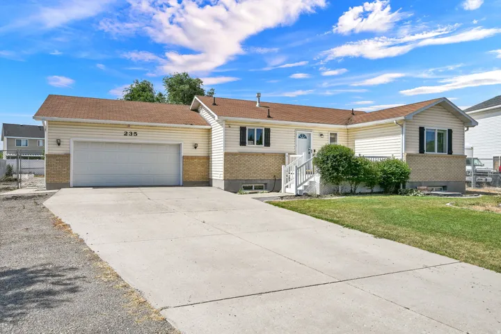 Ranch-style exterior featuring light-colored siding, brick accents, a two-car garage, concrete driveway, and a front entry porch with white railings