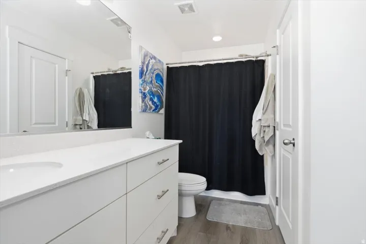 Bathroom featuring a white vanity with integrated sink, a large mirror, and wood-finish flooring