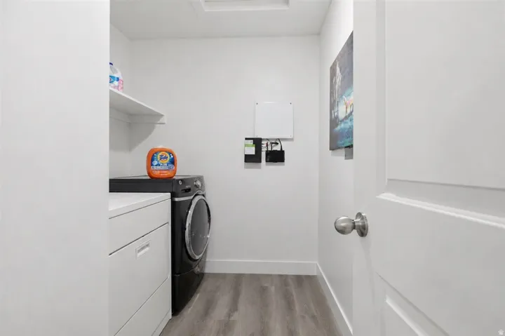 Laundry area featuring wood-finish flooring, white walls, and a built-in shelf