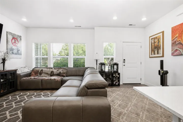 Spacious living area featuring bright white walls, recessed lighting, wood-finish flooring, and multiple windows providing ambient illumination