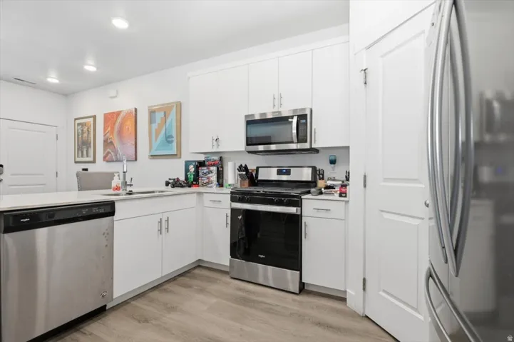 Modern kitchen featuring white cabinetry, stainless steel appliances, light-toned countertops, wood-finish flooring, and recessed lighting