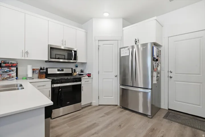 Contemporary kitchen with light wood-finish flooring, white cabinetry, and light-toned countertops