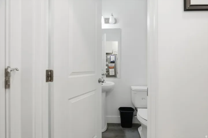 Powder room featuring a pedestal sink, white toilet, wall-mounted mirror, and overhead vanity lighting