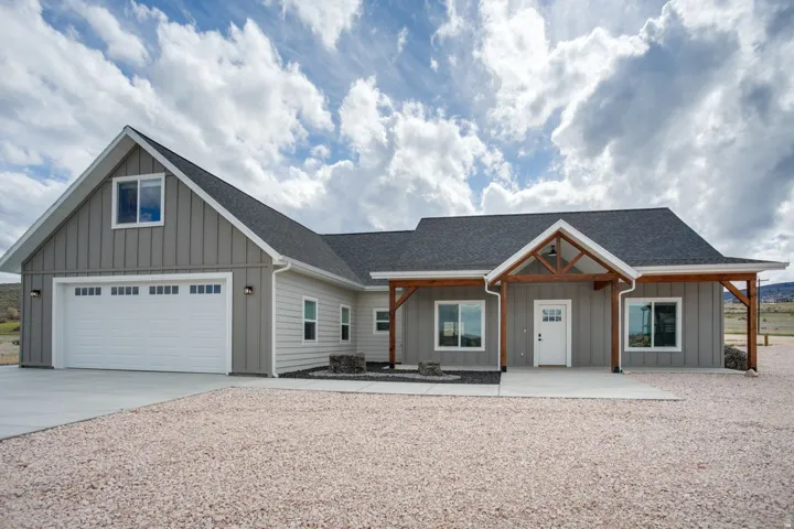 Contemporary exterior featuring light gray siding, dark asphalt shingles, a decorative timber frame porch, and an attached two-car garage with a white door