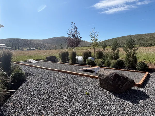 Gravel-covered outdoor recreation area featuring a built-in cornhole court with timber framing